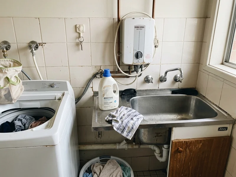 Compact instantaneous electric hot water unit mounted above a laundry trough